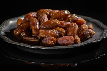 Sweet dessert dried date in old tin bowl, low key, dark theme, on black background with reflection