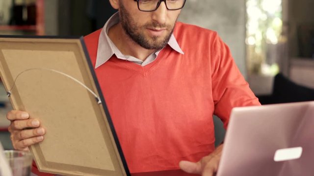 Young art curator looking and painting and checking something on laptop
