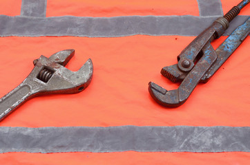 Adjustable and pipe wrenches against the background of an orange signal worker shirt