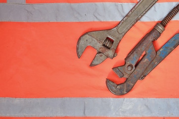 Adjustable and pipe wrenches against the background of an orange signal worker shirt