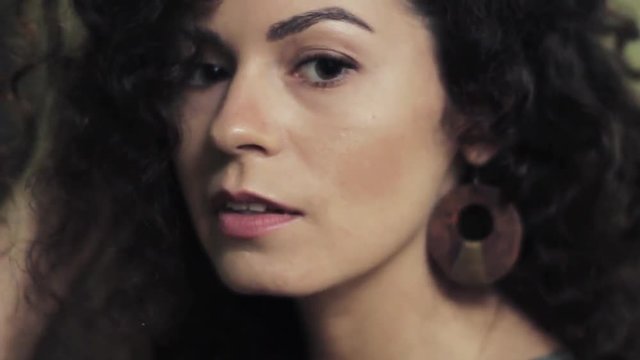 video portrait of a sensual girl with wooden earrings and green clothes. Flirting with the camera