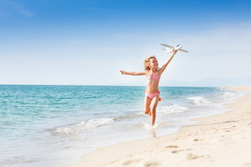 Fototapeta na wymiar Little girl running on the coast with toy plane