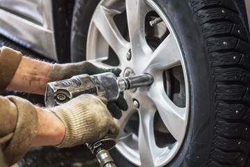 Car mechanic replace car wheels of lifted automobile by pneumatic wrench at repair service shop...