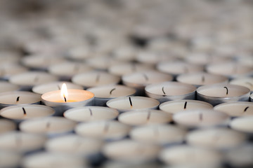 Naklejka premium Shining light from a solitary burning candle flame. Selective focus on one tealight among many.