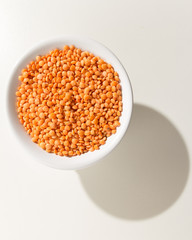 Turkish Red Lentil legume. Grains in a bowl. Shadow over white table.