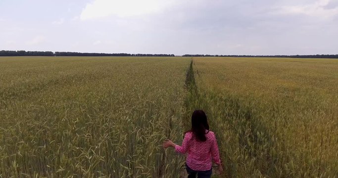 young beautiful girl is walking along the wheat field. happiness, nature, summer holidays, vacation and people concept - young woman.