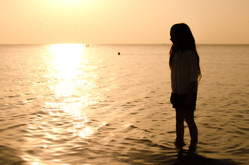 Fototapeta premium silhouette of a little girl standing in the water at sunset beach