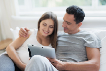 Fototapeta premium A pregnant woman and a man are lying on the bed. They are looking at something on their tablet