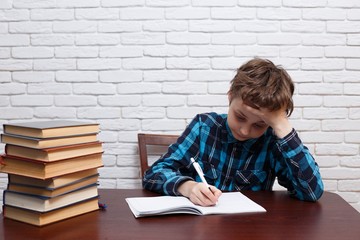 Stressed and exhausted pupil with torn papers sitting at the desk writing home task. Studying difficulties, education, school concept