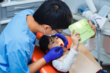 Dentist showing how to clean teeth to his little patient using a mirror. Pediatric dentistry,...