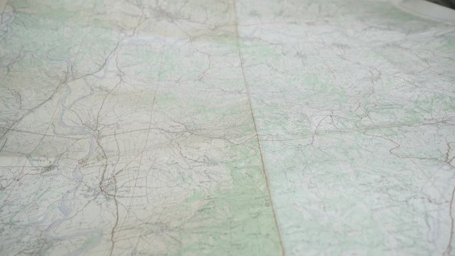 Group of young people holding and looking widespread geographical map, hikers showing with hands and fingers on relief, crane shot, motion close up from hands to wide angle view, concept hiking