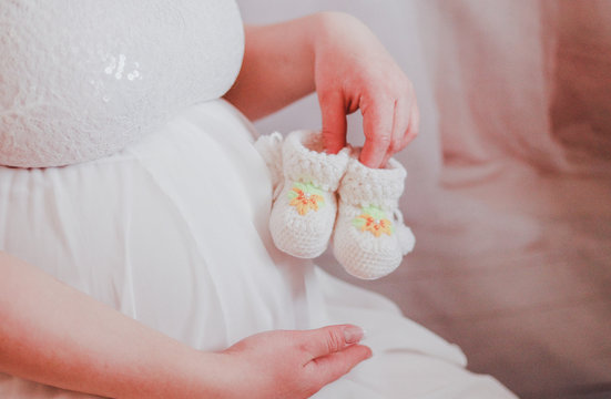 A pregnant woman holds the little booties for your unborn baby