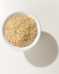 Whole Chinese Rice seed. Grains in a bowl. Shadow over white table.