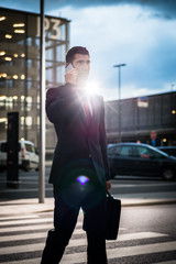 Fototapeta na wymiar Business man using phone in evening outdoors, picture has strong intentional lens flare