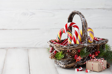 Christmas wicker basket with striped candy canes and gifts on white wooden table, festive decoration