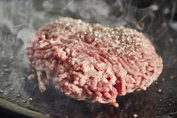 A hamburger patty frying on a cast iron grill