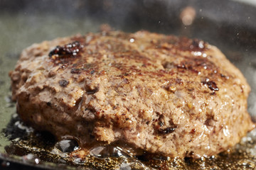 A hamburger patty frying on a cast iron grill