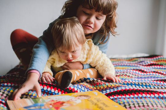 little girl and baby with a book on a bed