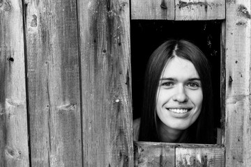 A young woman locked in a wooden shed, peeking through a small window. Black-and-white photo.