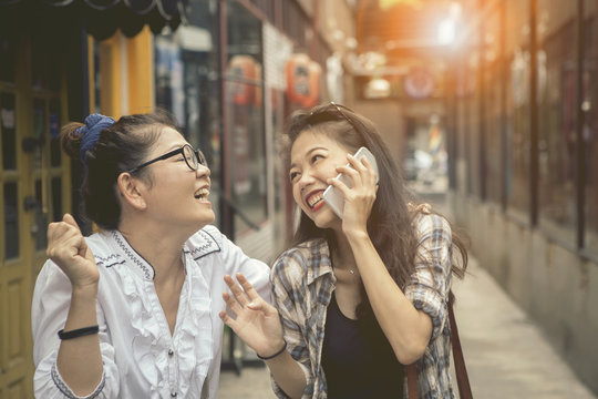 happiness emotion of asian two asian woman talking to smart phone and laughing in shopping street