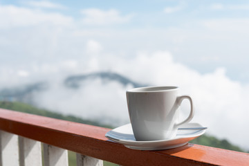 Close up white cup of hot coffee on balcony edge with outdoor natural green background