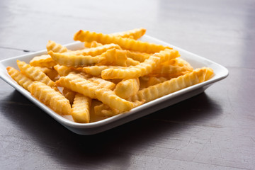 French fries in a white plate on a wooden table.
