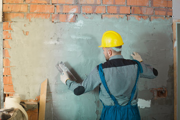 Professional worker in the helmet is plastering the wall