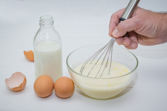 The man whips whisk milk and egg mixture with sugar.