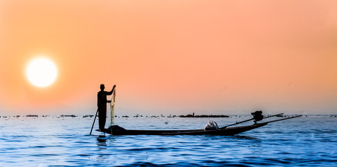 The illustration silhouette of the fisherman using the fishing net on a wooden boat at Inle lake, Taunggyi, Myanmar