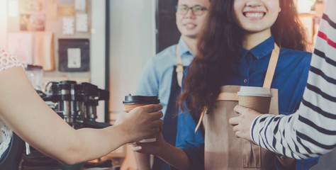 Young beautiful Asian woman barista wear brown apron holding hot coffee cup served to customer at bar counter in coffee shop with smile face.Concept of cafe and coffee shop small.