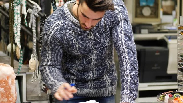 Handsome male shopkeeper keeping accountancy books in his store, writing on paper sheets and reading records