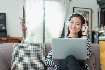 Asian teenager girl using laptop computer and listening music on sofa with happy smiling face at coffee shop,Digital age lifestyle