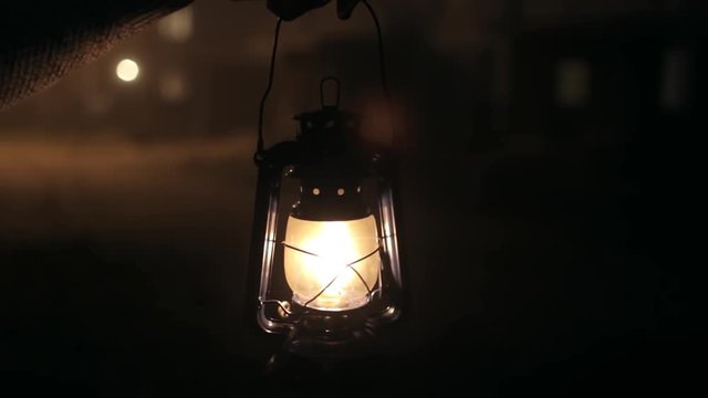 man's hand holds a lantern against a background of foggy street