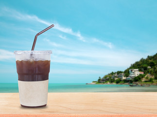 iced black coffee on  wooden table in the tropical paradise resort on the beach. the background for product display template