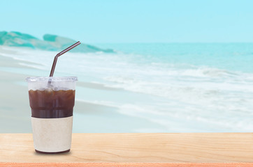 iced black coffee on wooden table in the tropical paradise beach. the background for product display template