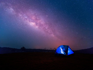 Camping. Blue tent glows under a night sky with milky way.