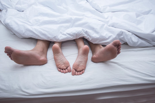 Close up legs of couple in bed.