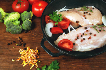 Raw chicken breast with vegetables ingredients in a cast iron skillet. Cooking