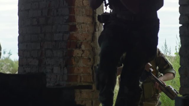 Tilt down shot of military men with weapons entering old destroyed building in slowmo