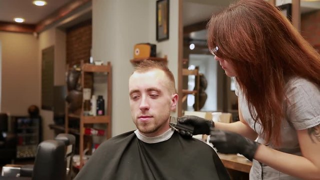 A woman Barber in the barbershop shop to put customer's man in a chair and begins to conduct his haircut.