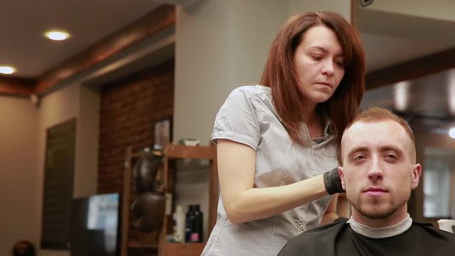 A woman Barber in the barbershop shop to put customer's man in a chair and begins to conduct his haircut.