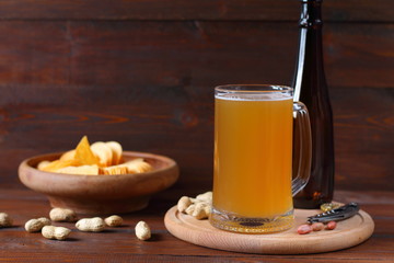 Mug of light beer and a bowl with chips on a dark wooden background. 