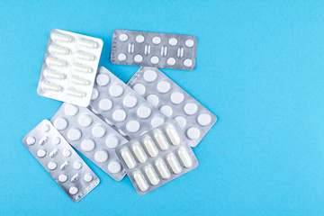 Packs of white capsules and pills packed in blisters with copy space on blue background. Focus on foreground, soft bokeh