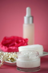 Obraz na płótnie Canvas A jar of luxury beauty face cream and serum bottle with pearls on pink color background with copy space. Styled feminine lifestyle image. 