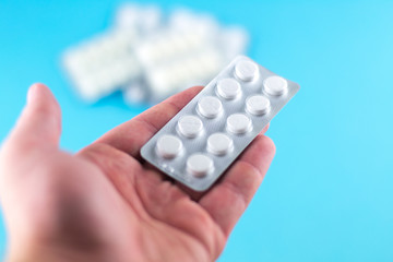 The man hand is holding a pack of white pills packed in blisters with copy space on blue background. Focus on foreground, soft bokeh
