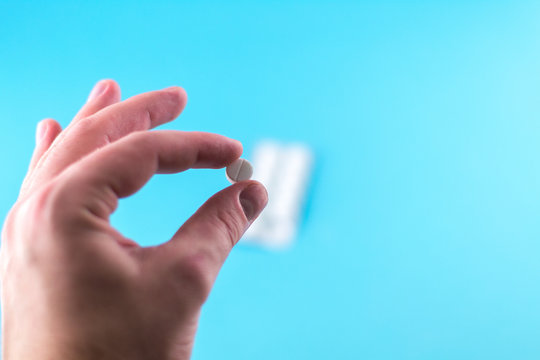 The man hand is holding a pill with copy space on blue background. Focus on foreground, soft bokeh