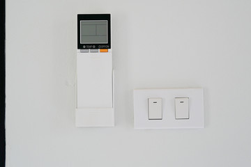 Air conditioner remote controller and light switches at a white painting concrete wall