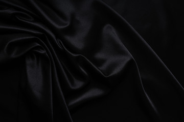 Dark black silky, satin  fabric, wave, draperies. Beautiful textile backdrop. Close-up. Top view 