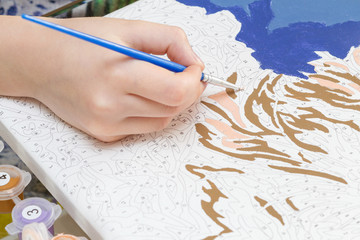 Young girl's hand draws with a brush painting by numbers on canvas. The concept of a hobby.