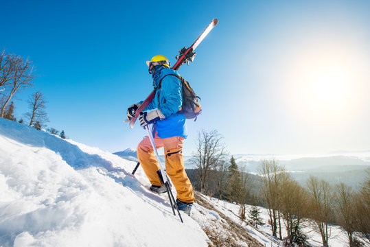 Shot of a male skier walking up the slope in the mountains carrying his skis copyspace active lifestyle equipment skiing concept. Blue sky and winter forest on the background